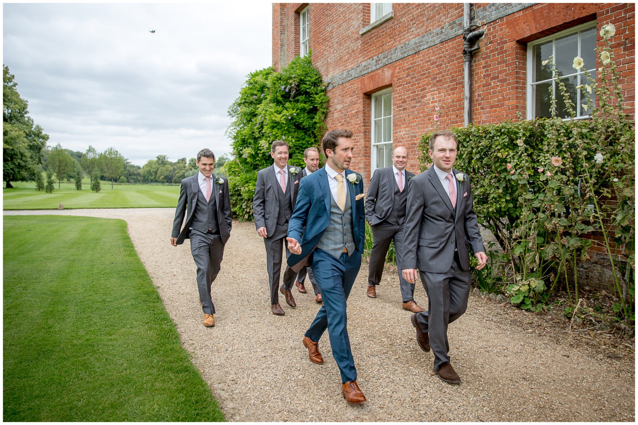 Groom, best man and ushers walk around the wedding venue towards the outdoor ceremony space