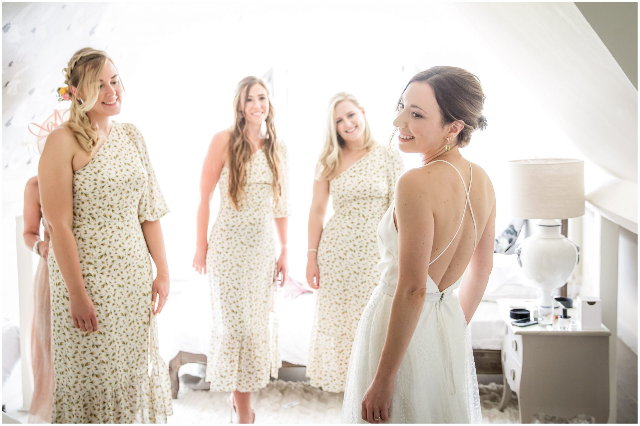 Bridesmaids watch and smile as bride tries on her wedding dress