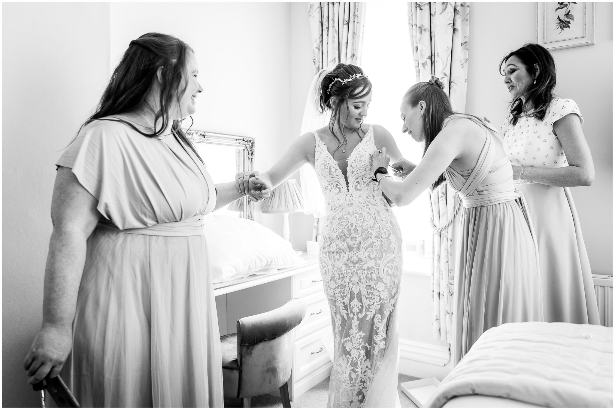 Bridesmaids help the bride get into her wedding dress black and white candid photography
