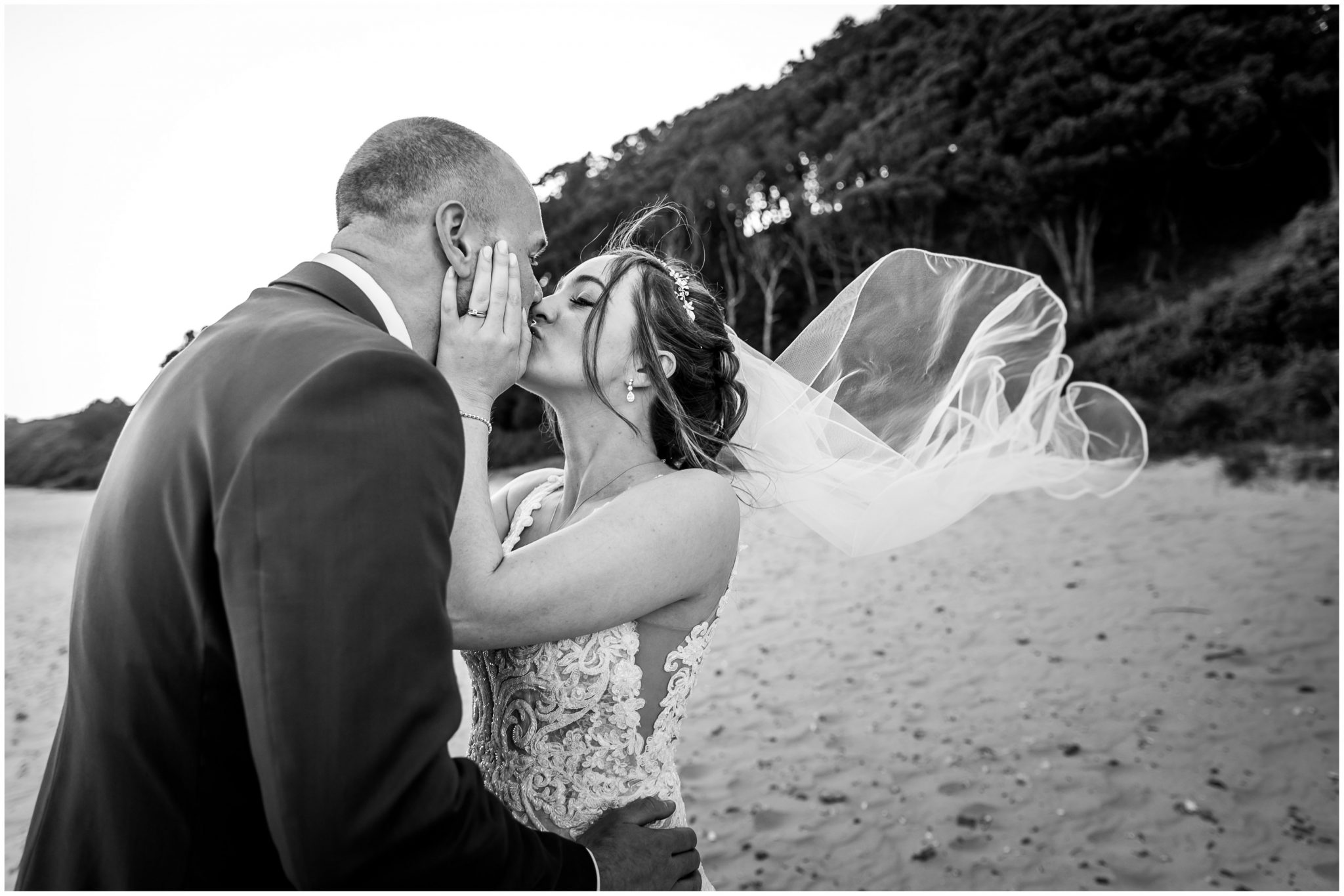 The couple kiss as the wind blows the veil on Highcliffe Beach Hampshire, black and white photograph
