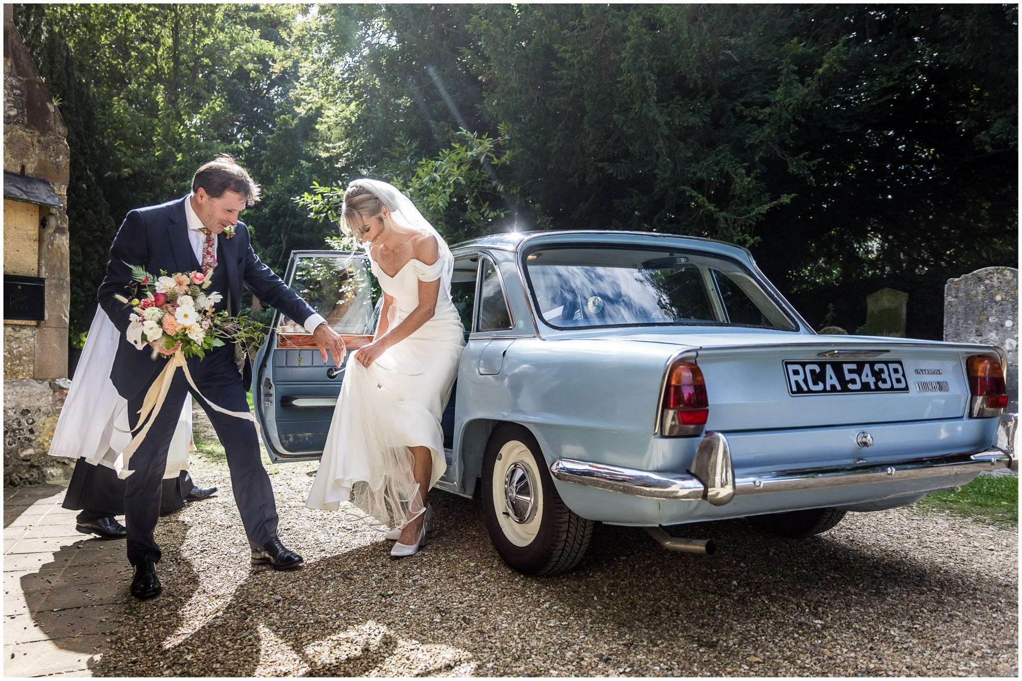 Father of the bride helps his daughter step out of the wedding car as they arrive at Droxford church