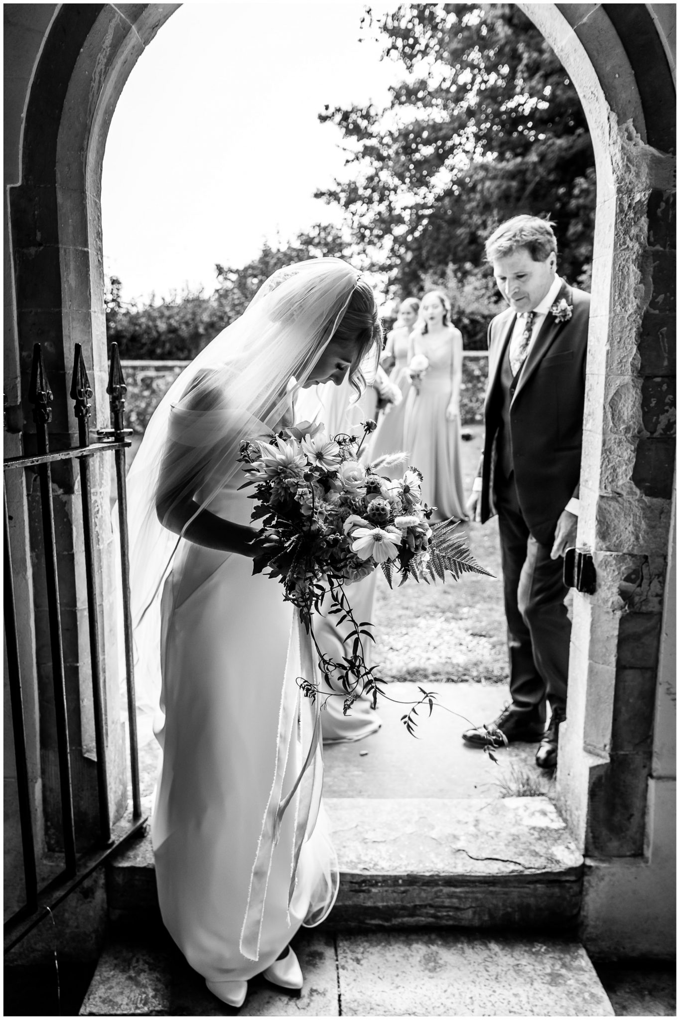 Black and white photograph of bride stood in the doorway to Droxford church, waiting to make her entrance