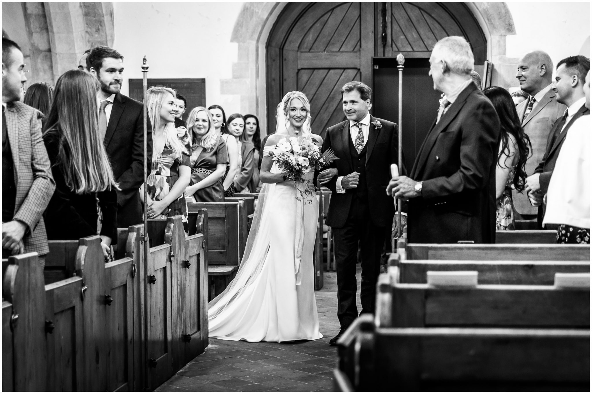 Black and white photo of bride walking down the aisle on her father's arm
