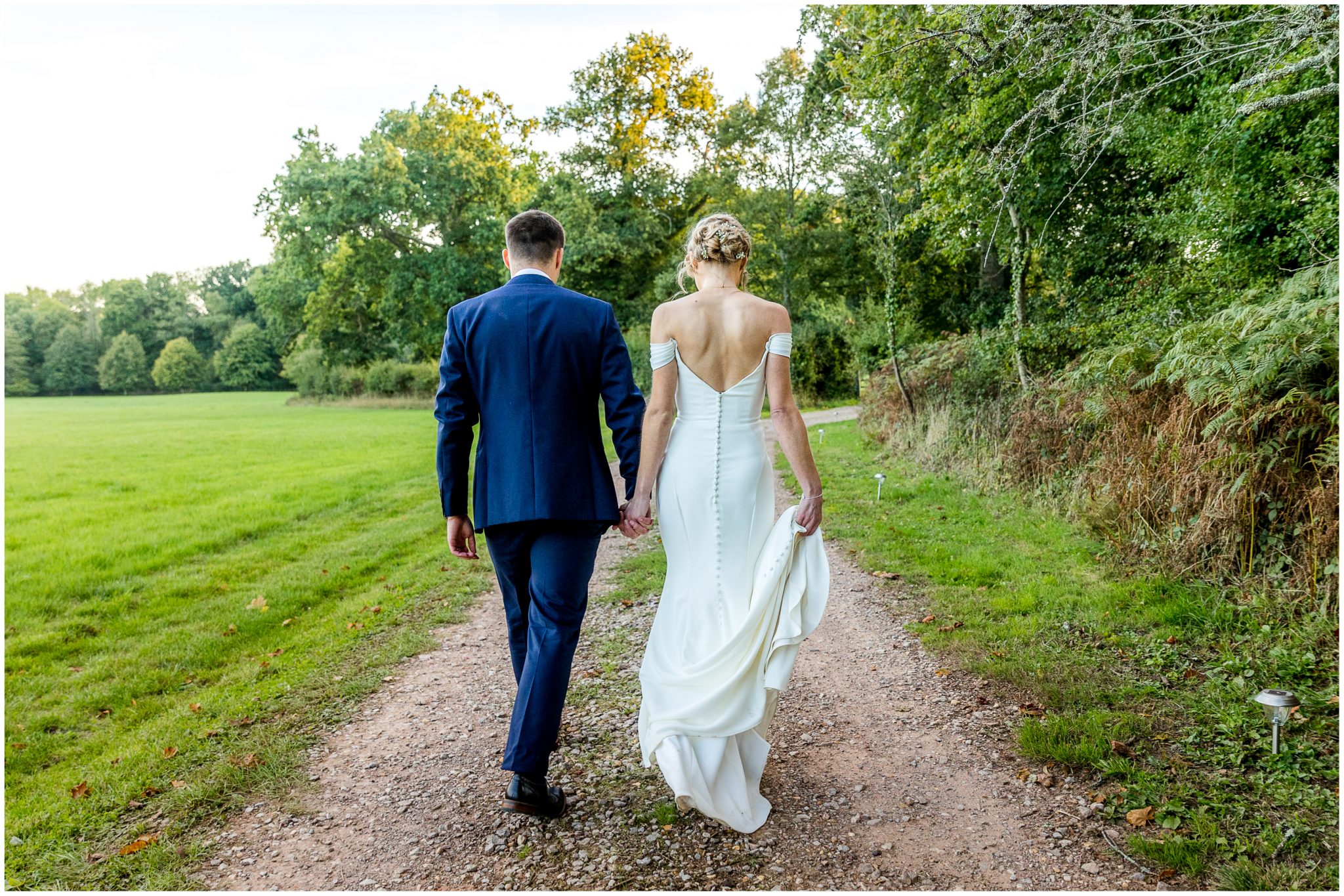 Bride and groom walk down a country track in the middle of the estate
