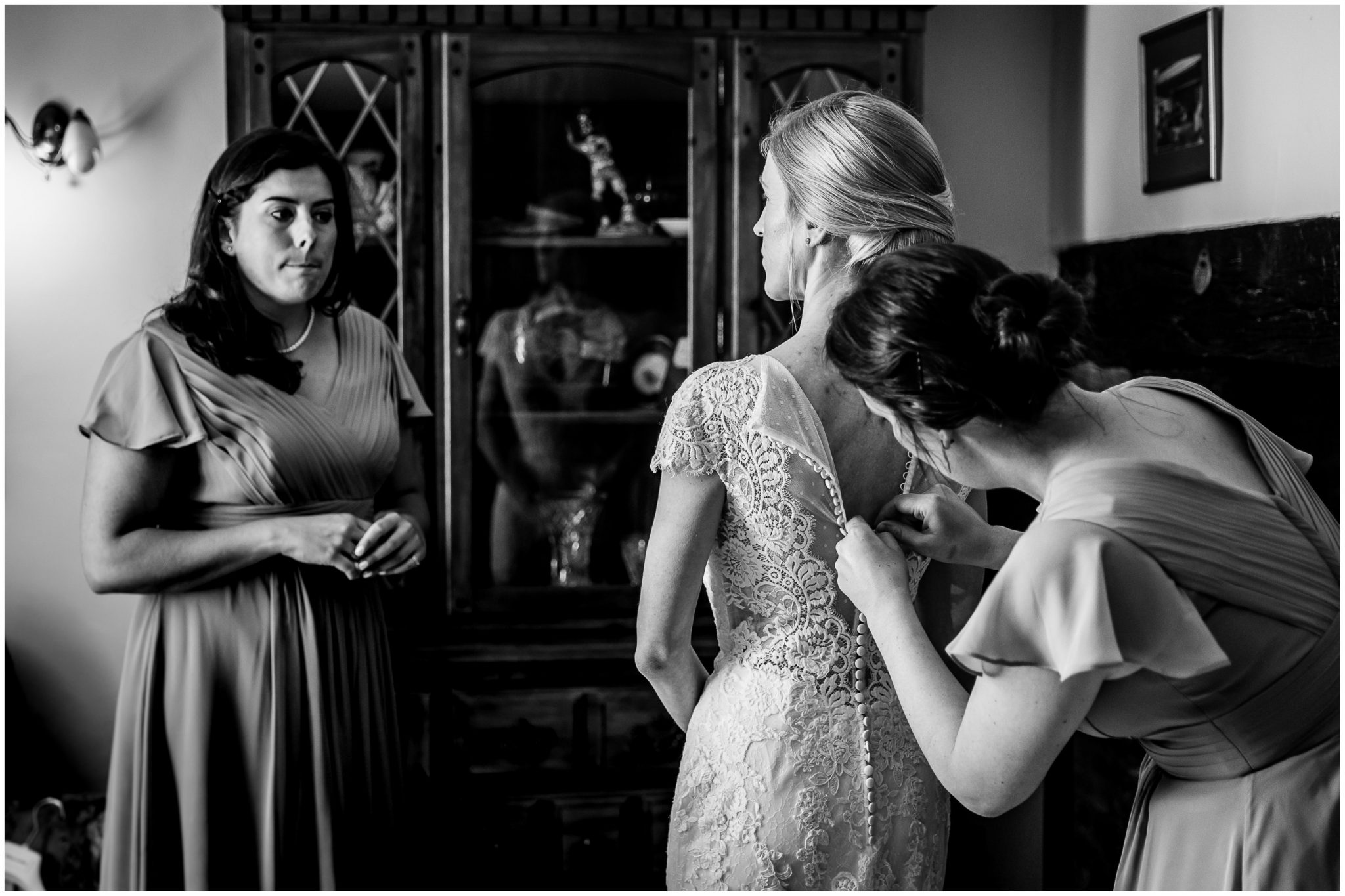 Bridesmaids help the bride into her wedding dress and do up the many buttons