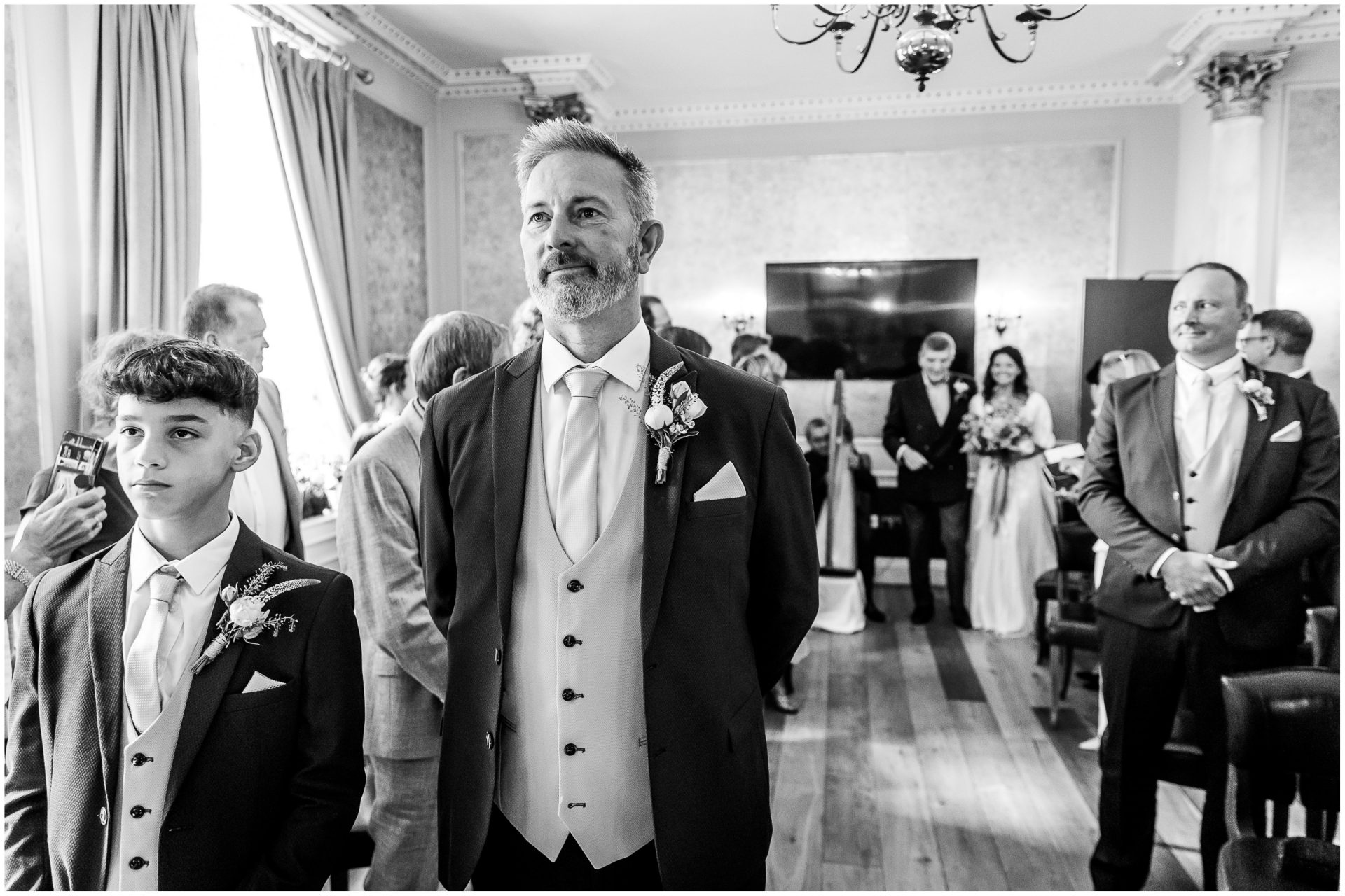 The groom stands at the front of the hotel's ceremony room as the bride walks down the aisle on her father's arm